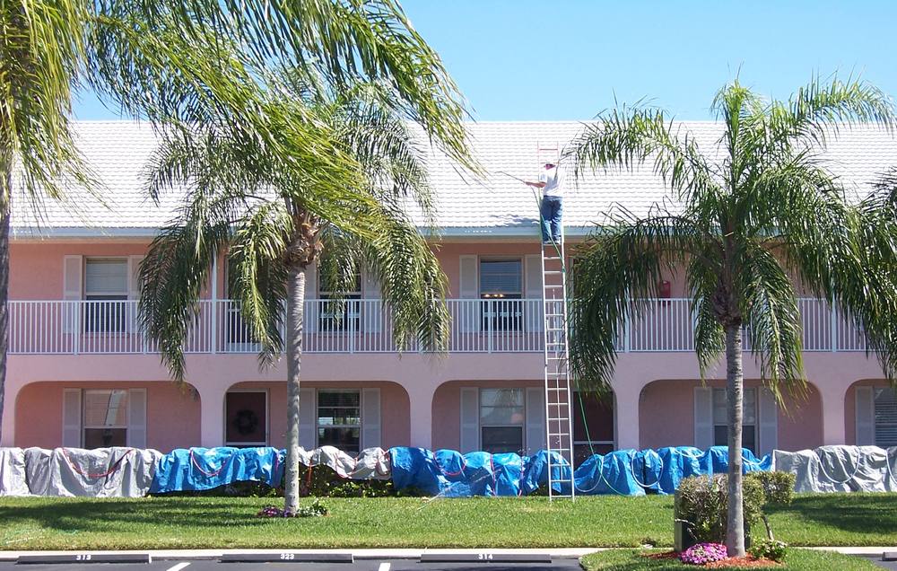 Two-storey condominium being cleaned from a ladder, with every planting bed tarped off below