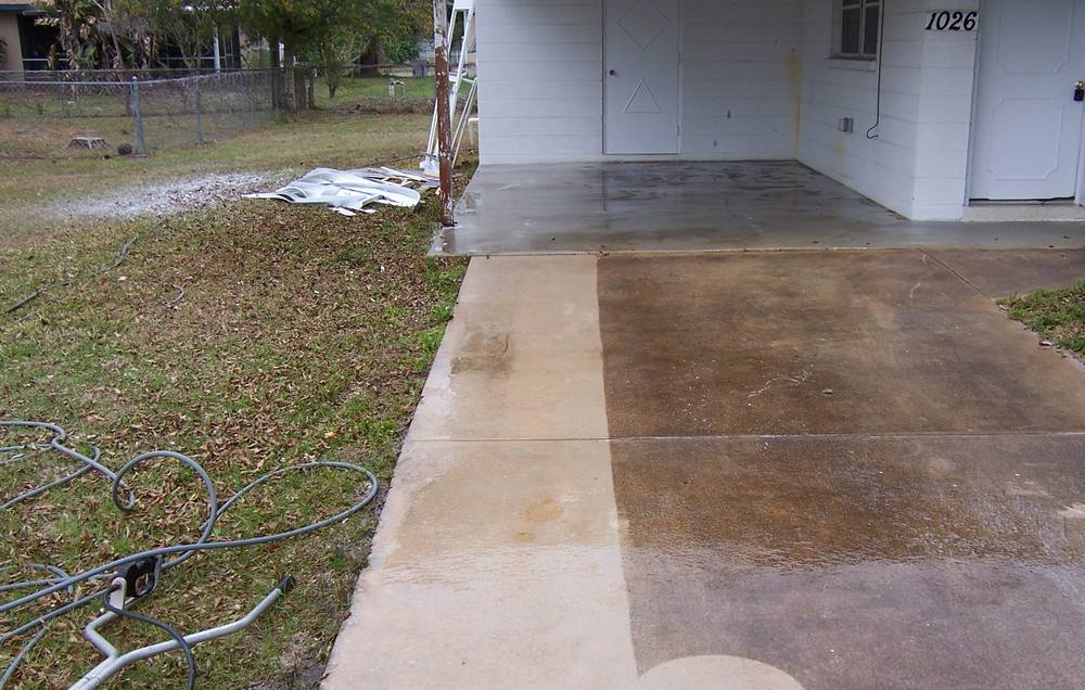 Concrete driveway mid-clean with the cleaned strip standing out against the stained slab